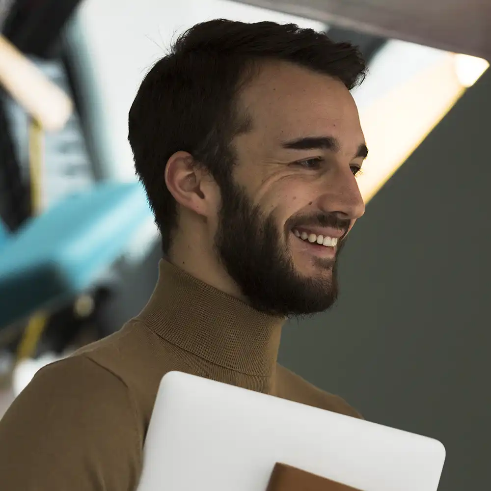 Student smiles with laptop and notebook. 