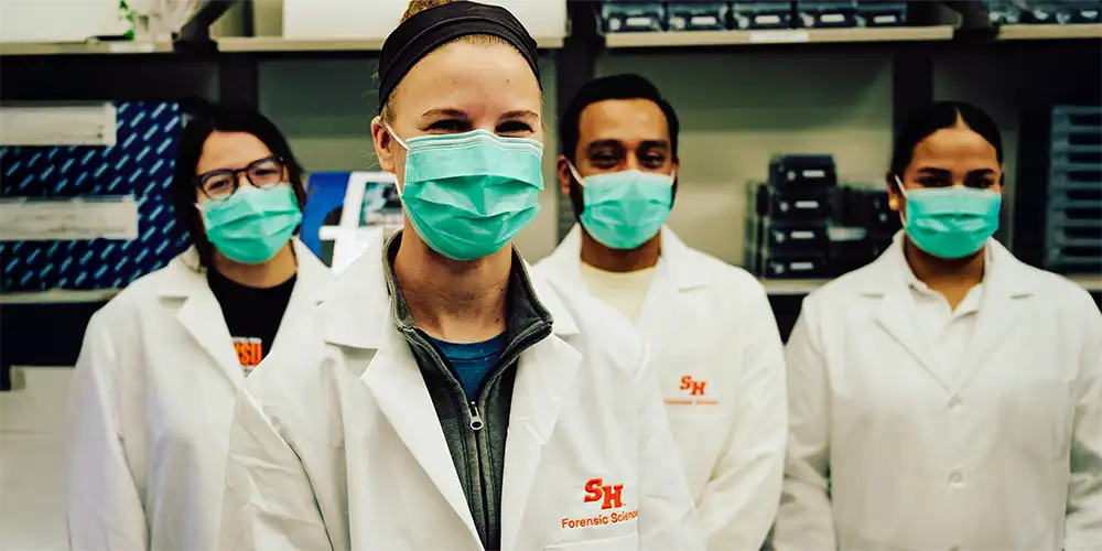 Forensic Science students wearing face masks and lab coats, standing in laboratory