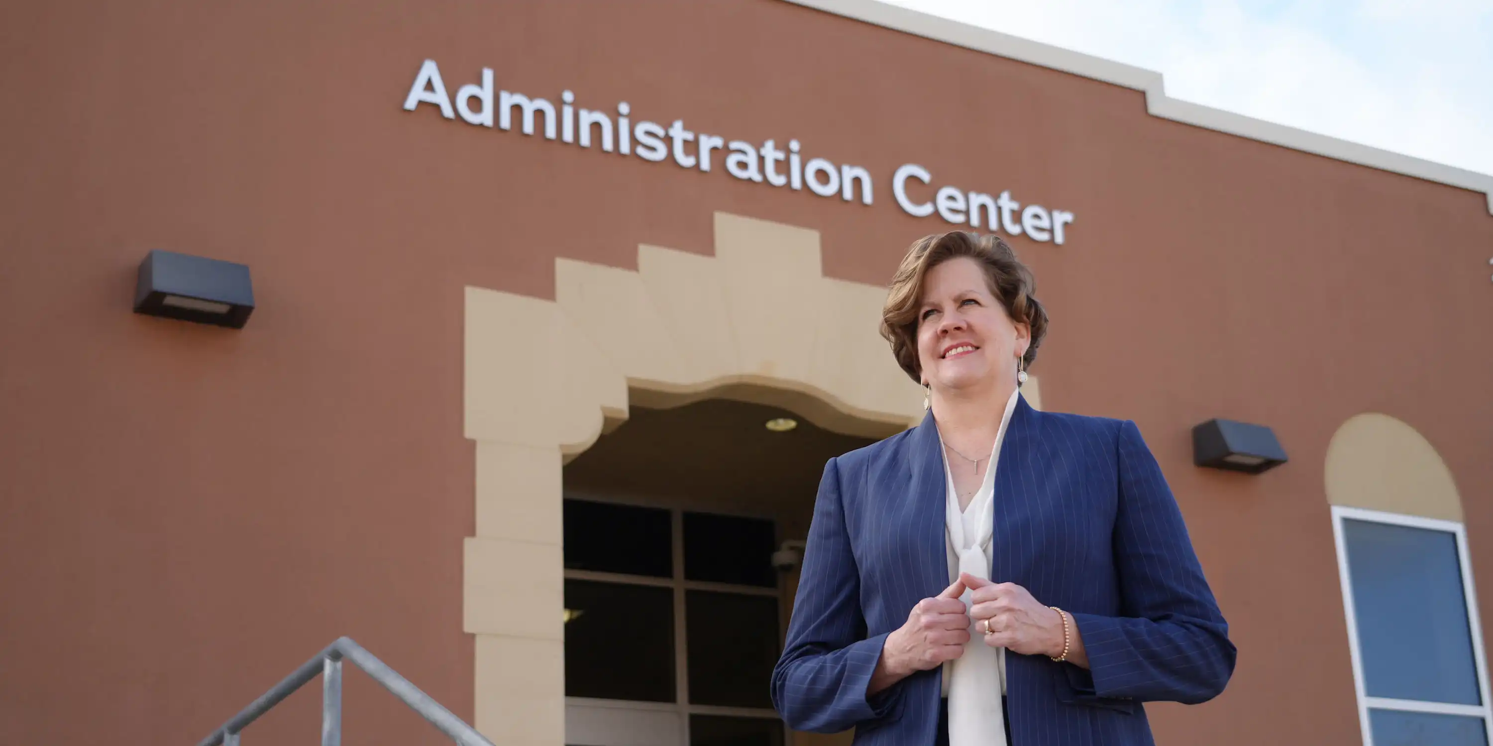 Sam Houston State University (SHSU) educational leadership program shows a woman in a suit smiling confidently while standing outside the Administration Center.