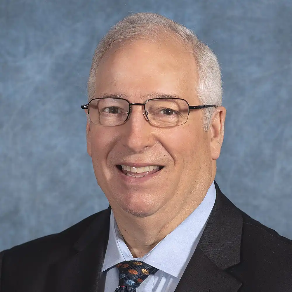 Smiling, older, white man in a suit with a color spotted tie.