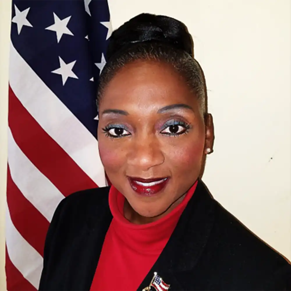 Smiling middle-aged woman with dark skin dressed in a red shirt, black blazer, and a military metal pined to it.