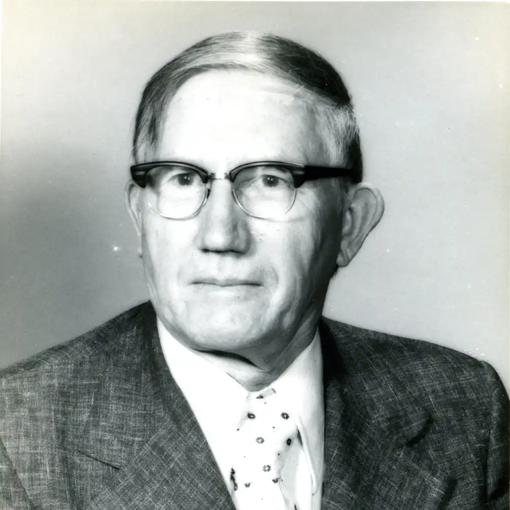 Black and white photo of an older white man in a suit with a polka dot tie.