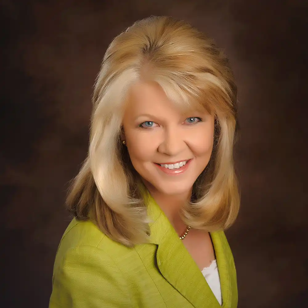 Smiling middle-age white woman with blonde hair in a green suit.