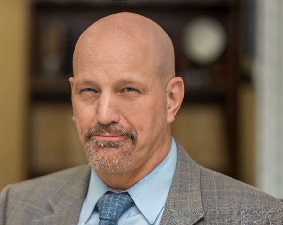 White male in beige suit and blue tie.