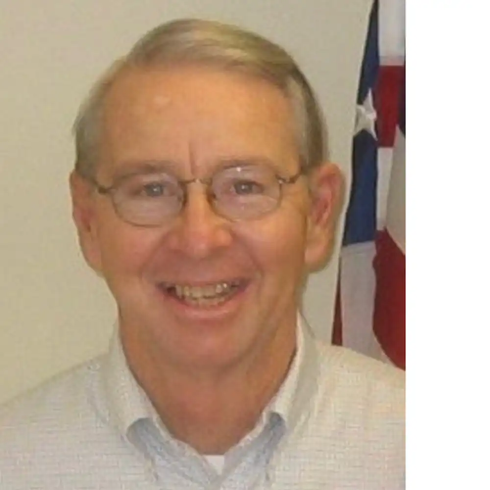 Smiling older white man in a beige button-up and glasses.