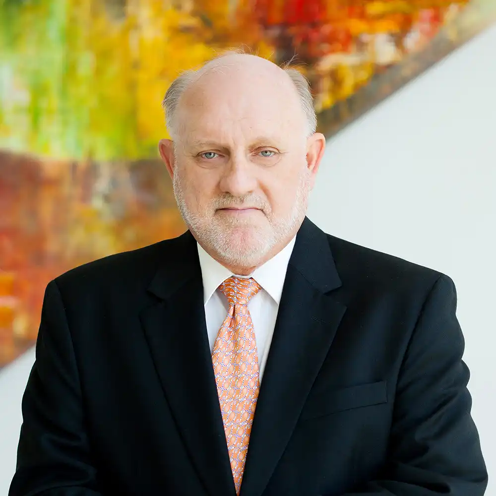 Older white man in black suit with a an orange tie poses in the stairwell of the College of Humanities and Social Sciences building.