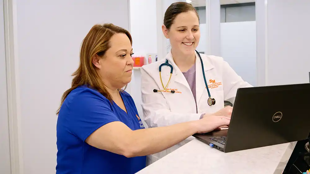 A doctor looking at her computer smiling while a nurse points at something on the screen