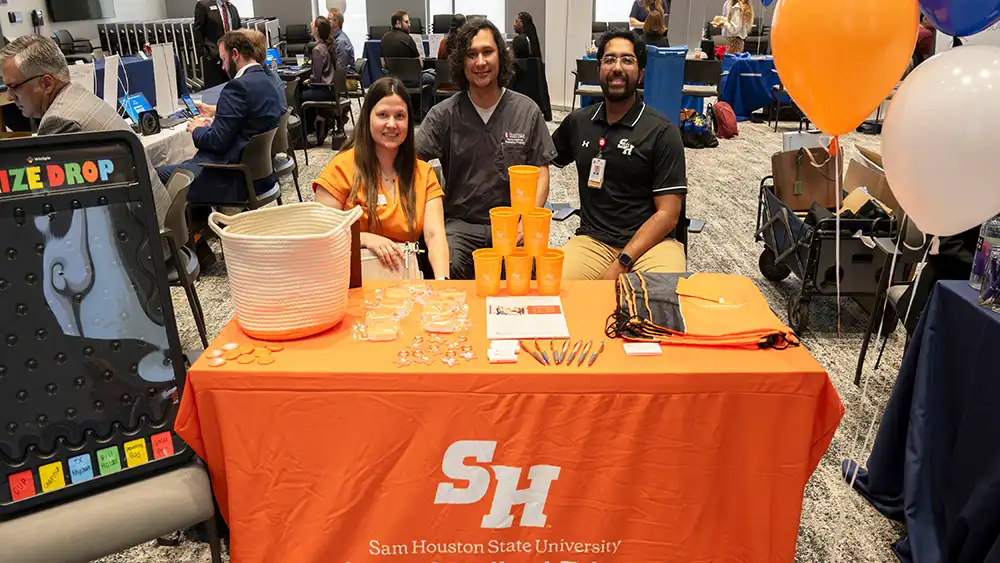 Three members of the GME team behind a table at an exhibition