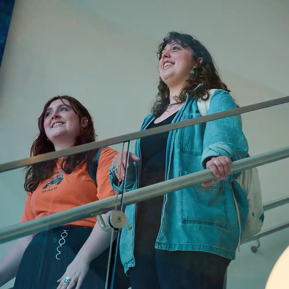 Two women looking at each other, smiling, sitting down, working on an assignment.