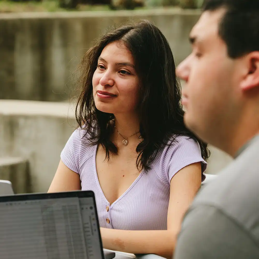 Two women looking at each other, smiling, sitting down, working on an assignment.