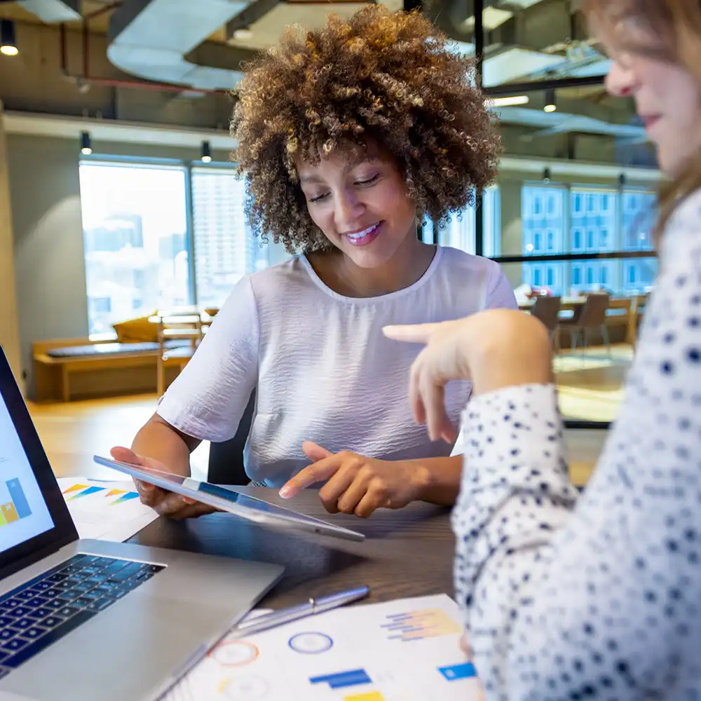 Two women looking at each other, smiling, sitting down, working on an assignment.