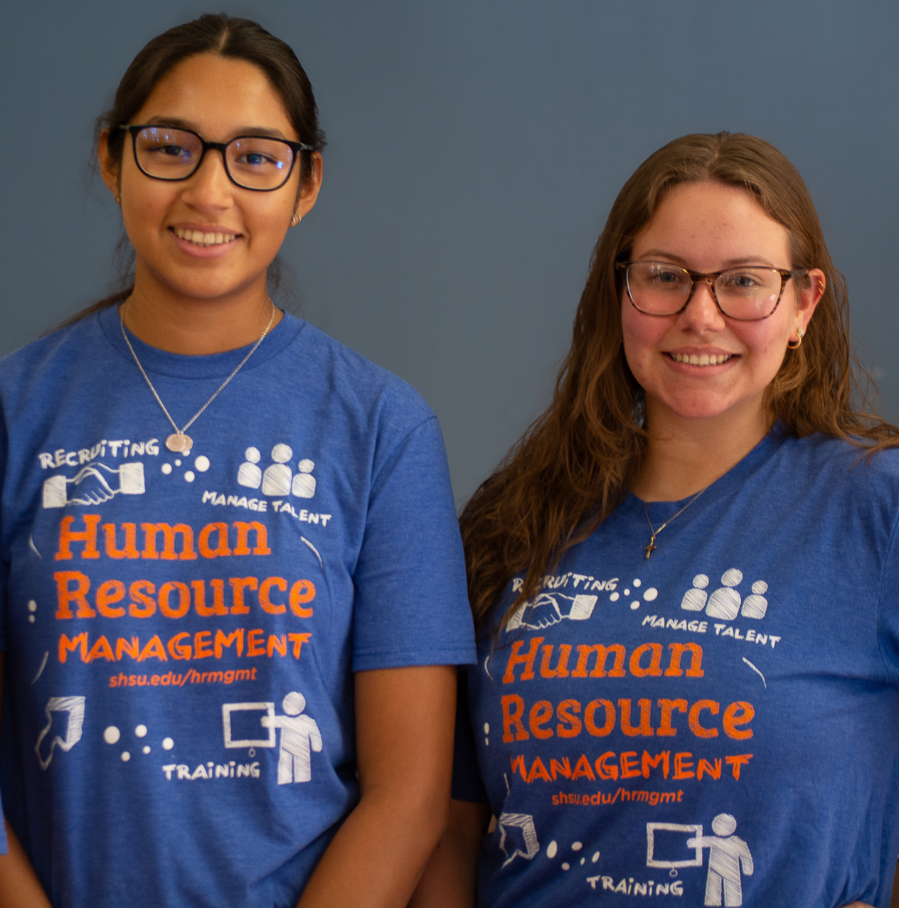 Two women looking at each other, smiling, sitting down, working on an assignment.