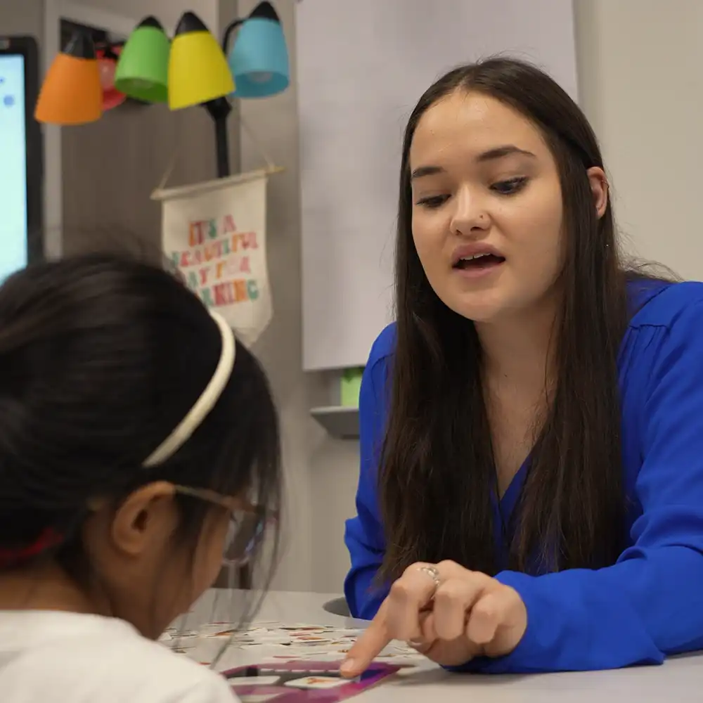 Two women looking at each other, smiling, sitting down, working on an assignment.