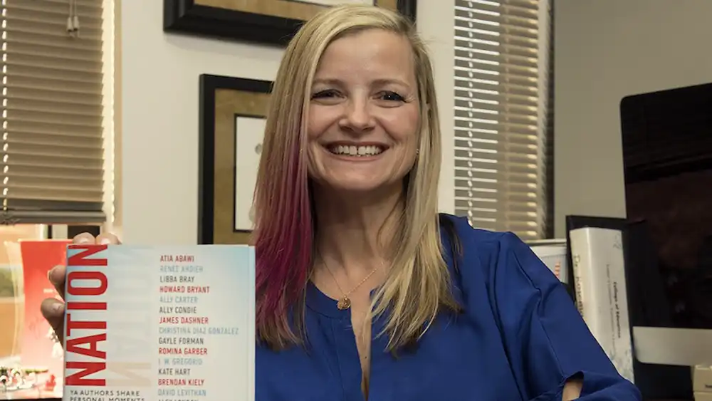 Professor speaking to the camera in a classroom style class, with her hands opened.