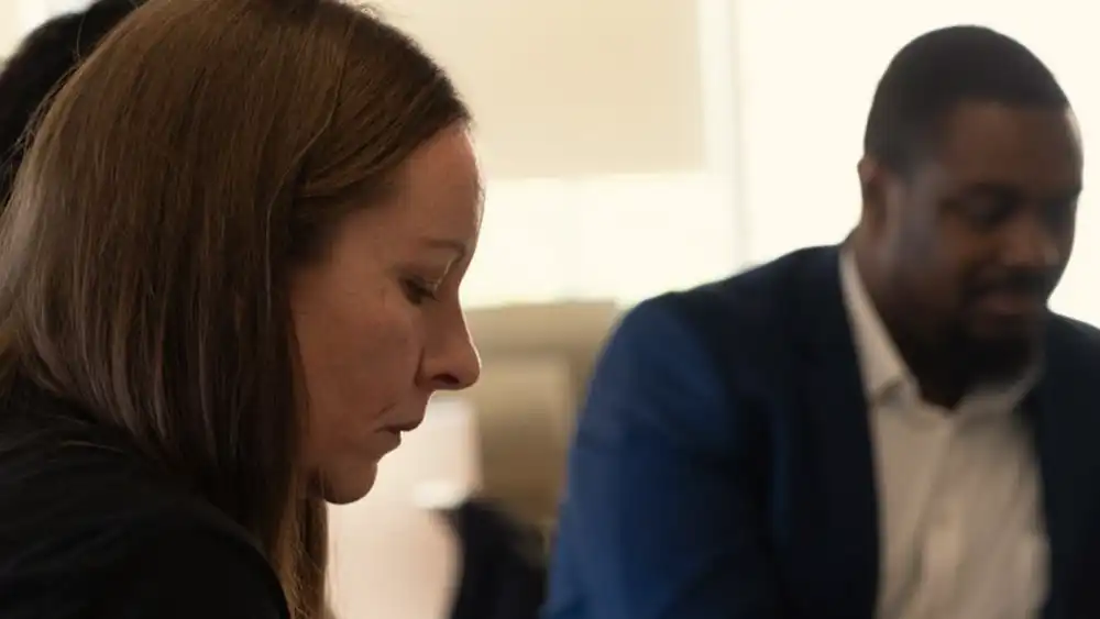 Professor speaking to the camera in a classroom style class, with her hands opened.