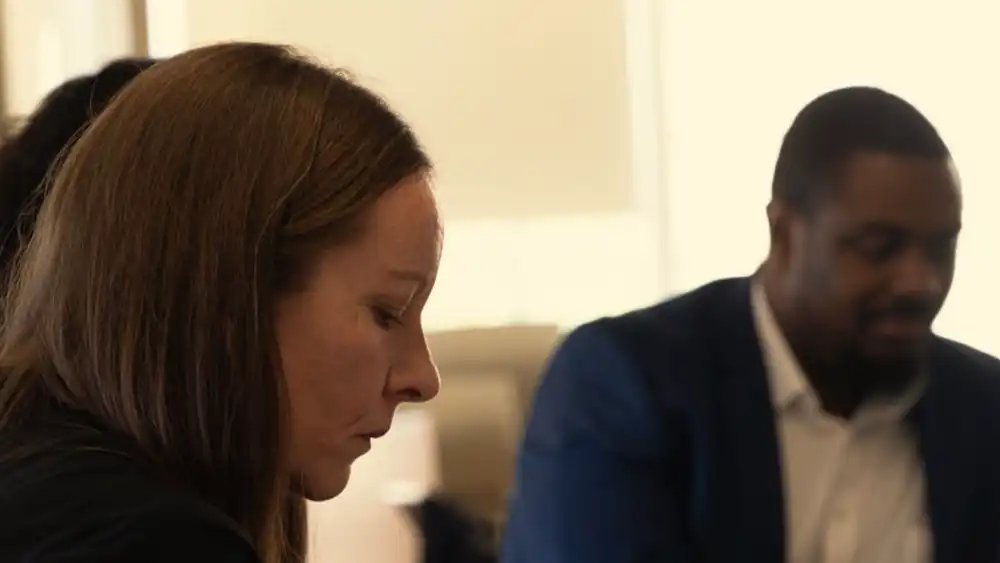 Professor looking down, writing, while in a meeting with other people.