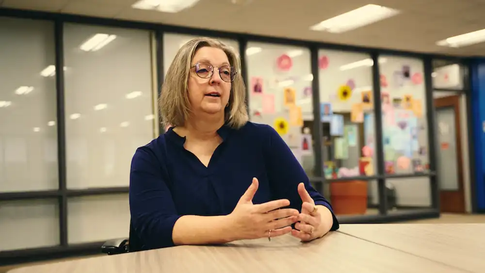 Professor speaking to the camera in a classroom style class, with her hands opened.