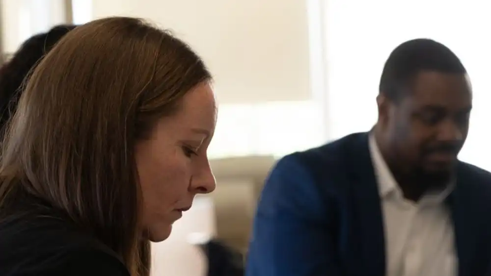 Professor looking down, sitting down with people around her, focusing on her work