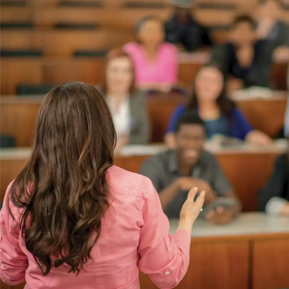 Woman standing at the front of a lecture hall speaking to students