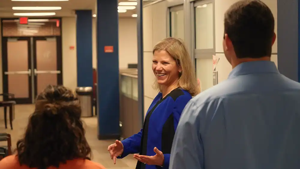 Woman smiling, talking to people behind her.