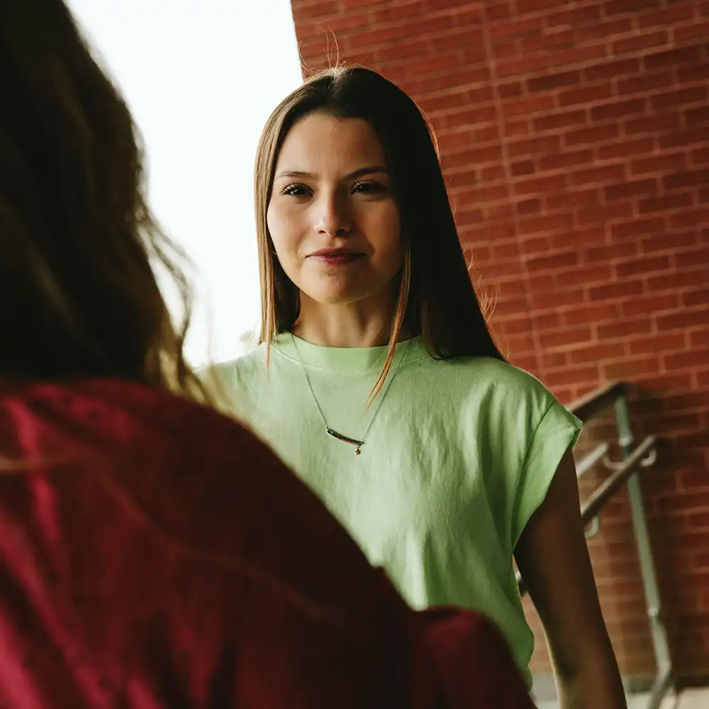 Two women looking at each other, smiling, sitting down, working on an assignment.