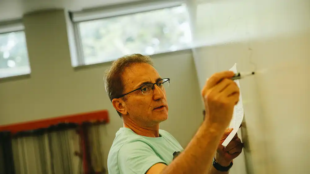 Professor speaking to the camera in a classroom style class, with her hands opened.