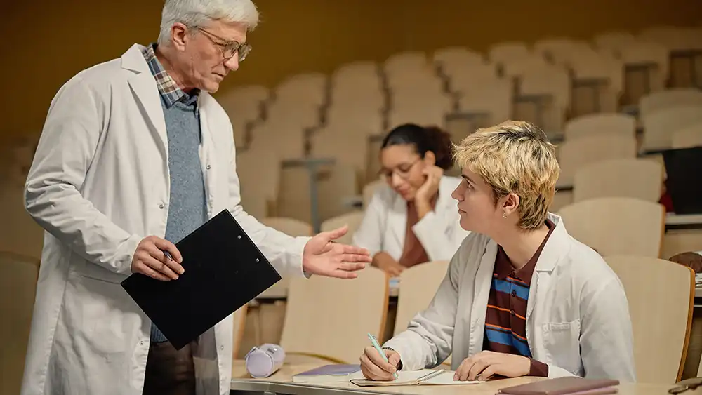 Professor speaking to the camera in a classroom style class, with her hands opened.
