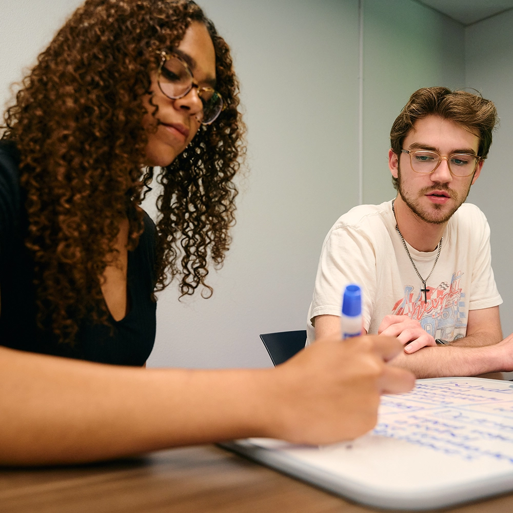 Undergraduate students writing on whiteboard on table in classroom