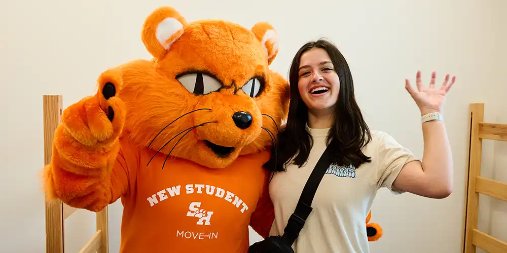 Student making a Bearkat paw and smiling with Sammy.