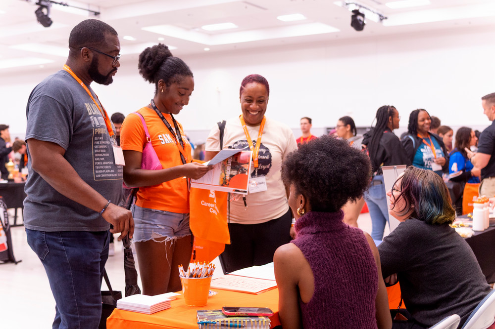 Parents smile as their student talks to people tabling at New Student Orientation.