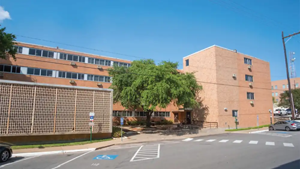 Exterior view of Estill Hall at Sam Houston State University, a multi-story brick residence hall with shaded entry, large windows, and nearby accessible parking.
