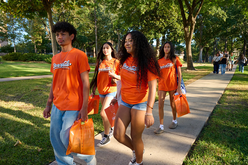 four students in orange shirts walking a path on shsu's campus