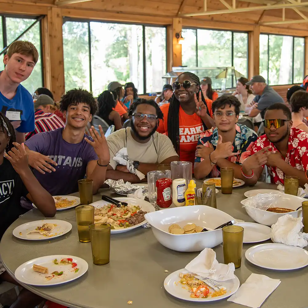 Students posing for the picture while they sit around a table eating fajitas in a well-lit indoor building. 