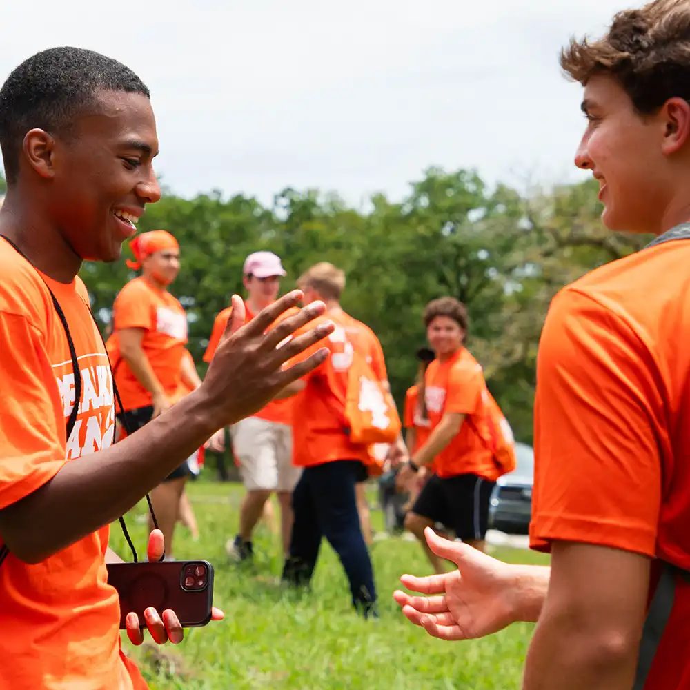 Two students wearing orange “bearkat camp” shirts going in for a handshake with other students in the background. 