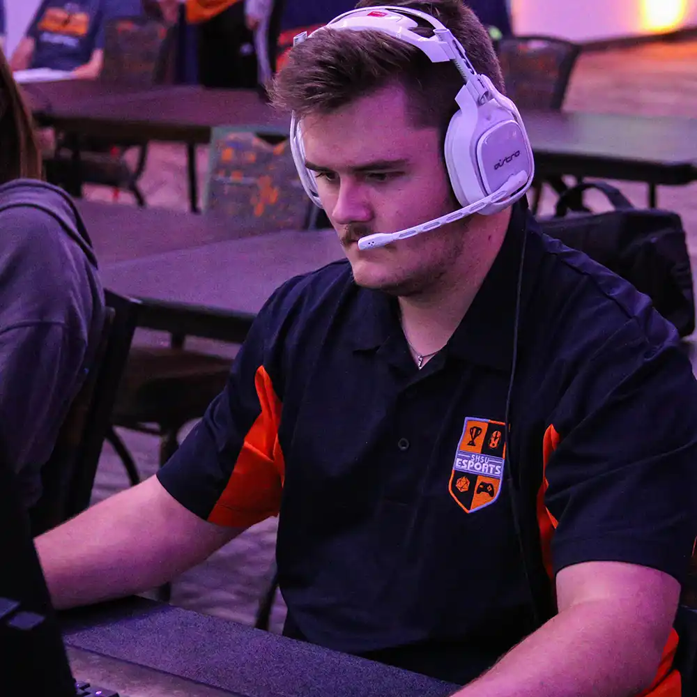 Young guy wearing a white headset playing a video game on a computer monitor.