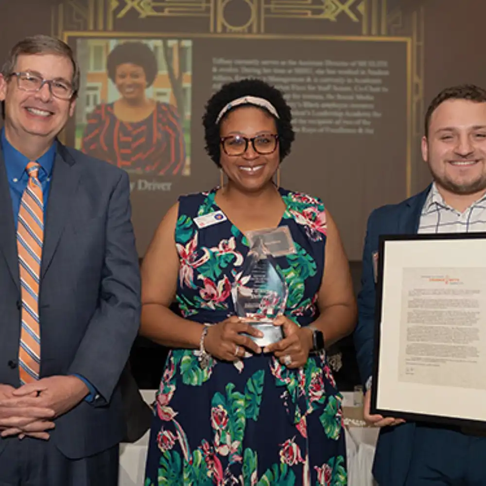Woman standing with two men after receiving the Keys of Excellence award.