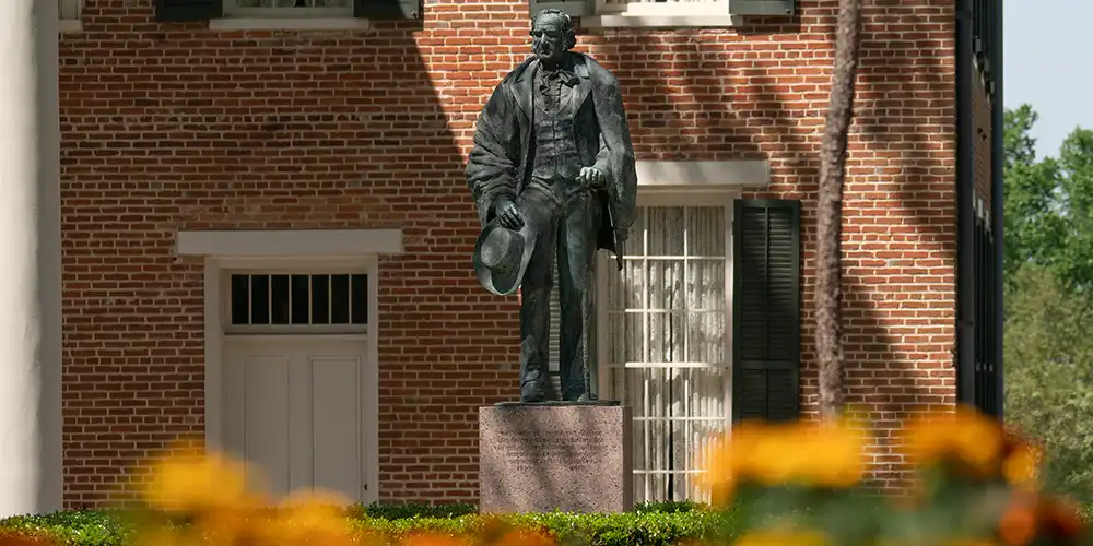 Statue of Sam Houston in front of historic campus building with flowers in foreground