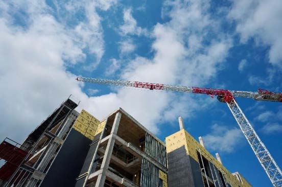 Construction crane over the future Health Professions Building, with exposed concrete and insulation panels against a blue sky.