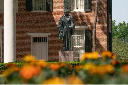 Bronze statue of Sam Houston outside Austin Hall, surrounded by a garden with bright orange and yellow flowers.