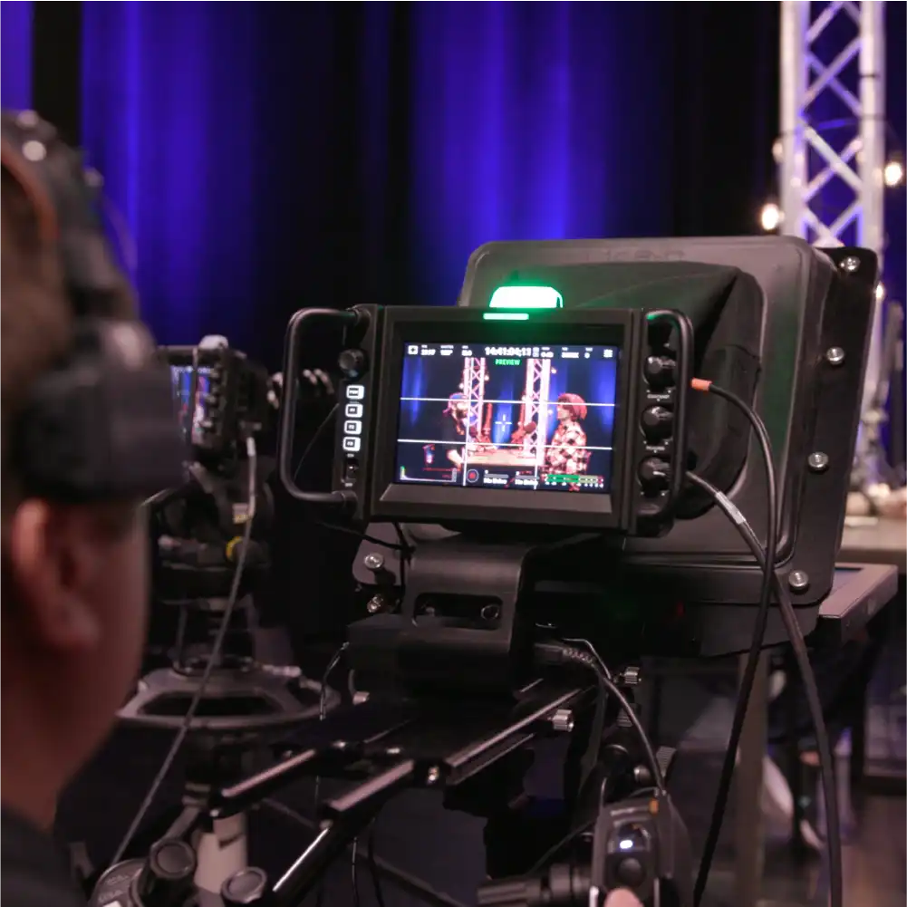 Camera operator filming two people in a studio with microphones and blue stage lighting.
