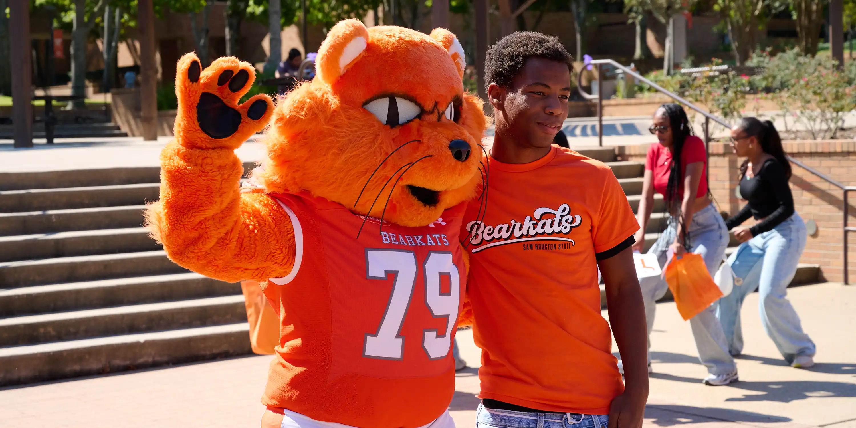 Sammy Bearkat standing with a student holding SHSU penant with hand up in claw form.